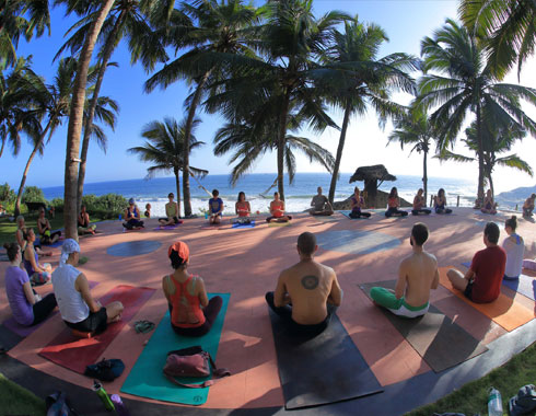 Group of people practicing yoga next to a beach.