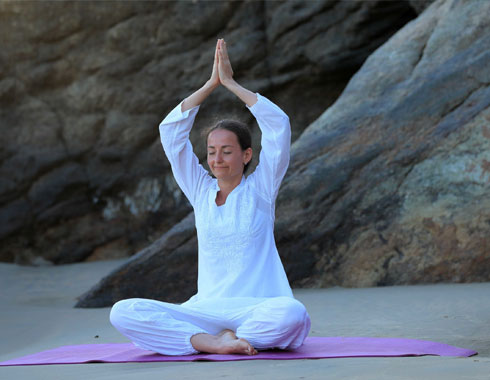 Woman practicing yoga on a beach with rocks in the background.