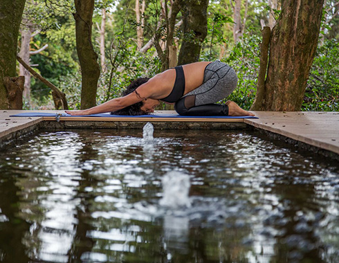 Woman practicing yoga next to a pool.