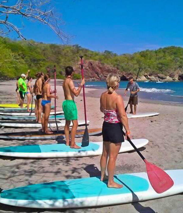 Group of people following a stand up paddle board class.