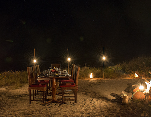 Dressed table, chairs and lights on a beach.
